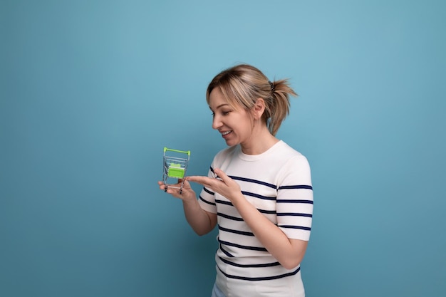 Horizontale foto van een jonge vrouw die shopaholic is met een winkelwagentje op een blauwe achtergrond met kopie