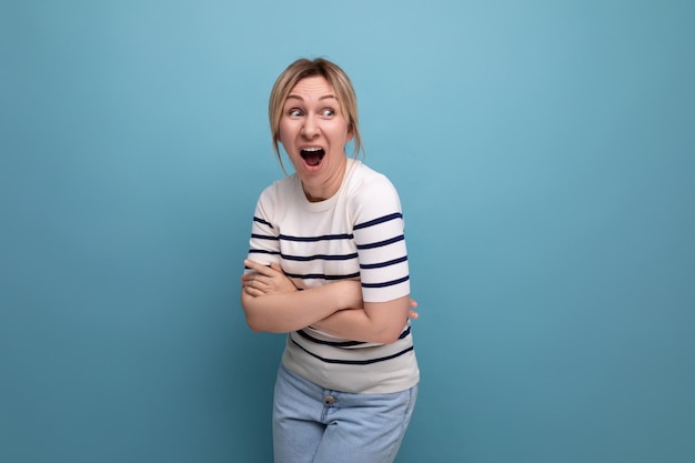 Horizontale foto van heldere vrolijke gelukkige blonde vrouw in casual outfit op blauwe achtergrond met kopie