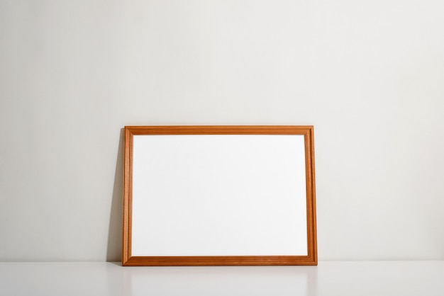Horizontale houten frame mock-up met lege ruimte voor foto of schilderij, staande tegen de muur op witte tafel binnenshuis. Minimaal interieur met lay-outelement.