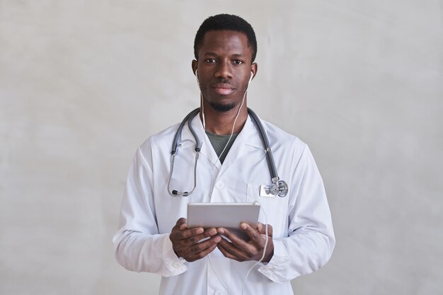 Horizontale, middelgrote portretfoto van een knappe zwarte dokter die een koptelefoon draagt met een digitale tablet vast