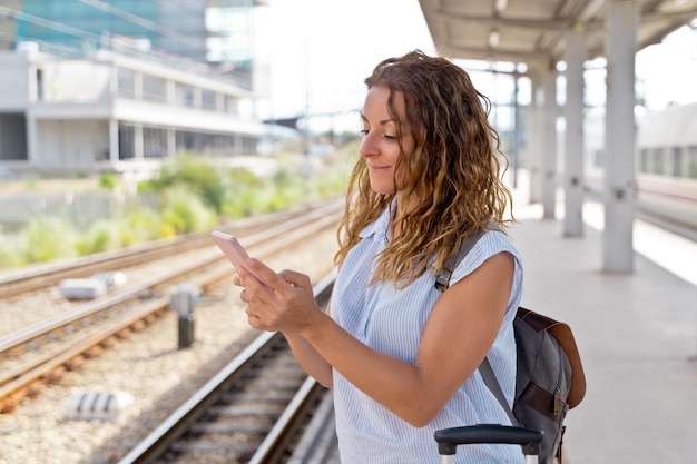 Horizontale weergave van vrouw in treinplatform met smartphone. Blanke vrouw die technologie gebruikt en met het openbaar vervoer reist. Reizen en technologie concept.