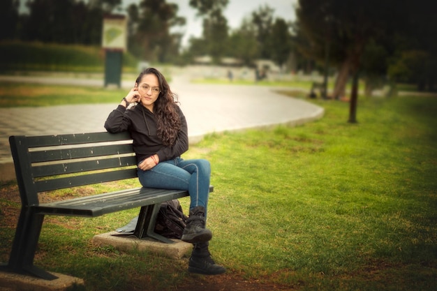 Horizontale weergave waar een jonge vrouw op de voorgrond zit op de bank in een heel groot park en op de achtergrond een heel mooie lucht