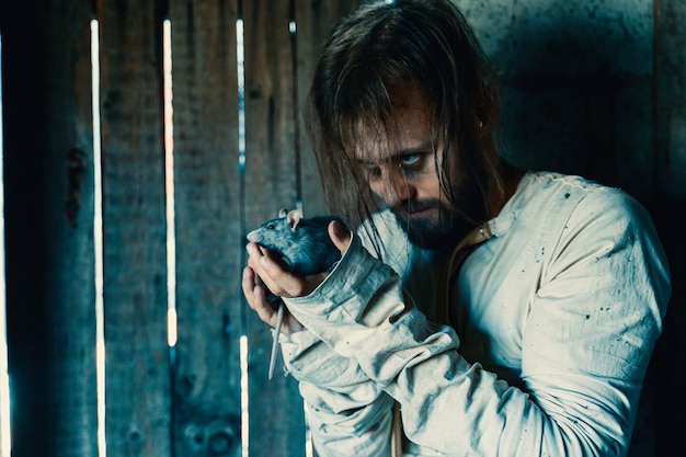 Horror for halloween holiday crazy man in a dirty measuring\
shirt in an old ruined house is locked and scares everyone\
surrounding expecting a victim with rat