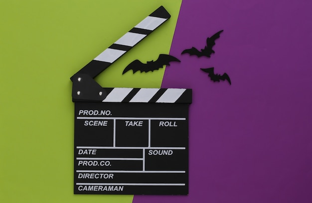 Horror movie, halloween theme. Movie clapperboard and flying decorative bats on green purple