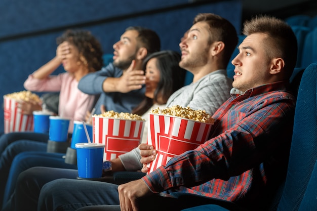 Horror movies marathon. Young man looking scared sitting at the movie theater with his friends