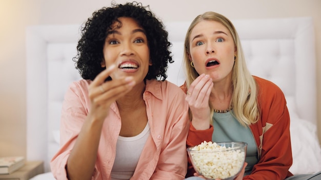 Horror television and women friends with popcorn on bed for scary movie or serial killer documentary at home Watching tv face and ladies in bedroom with terror film or video snack and streaming