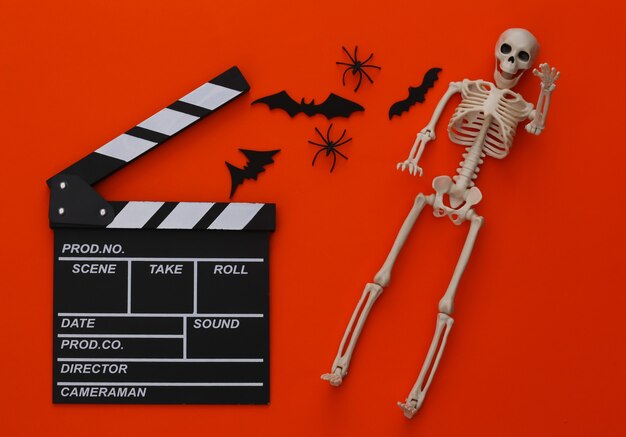 Horrorfilm, Halloween-thema. Filmklapper, skelet, spinnen en vliegende decoratieve vleermuizen op oranje