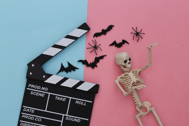 Horrorfilm, Halloween-thema. Filmklapper, skelet, spinnen en vliegende decoratieve vleermuizen op roze blauwe pastel