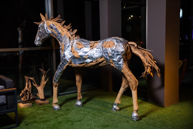 A horse made of aluminum and silver tape sits in front of a window.