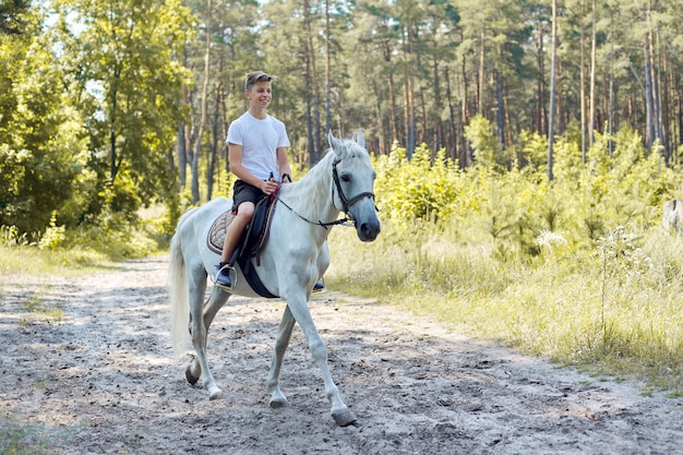 Passeggiate a cavallo, ragazzo adolescente a cavallo bianco nella foresta di estate