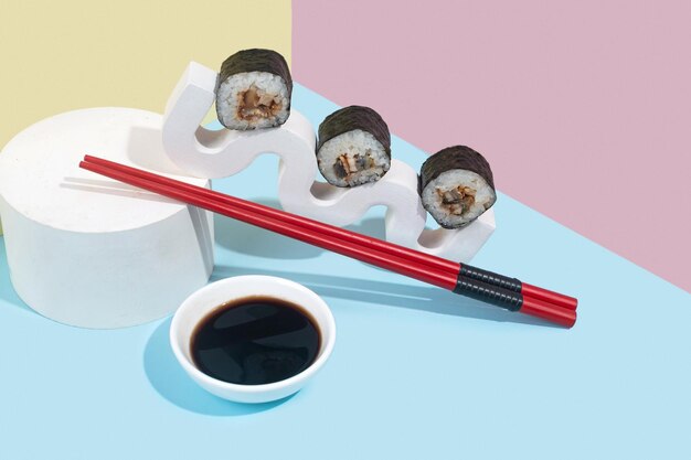 Hosomaki sushi rolt met paling en sojasaus op een witte gipsstandaard op een kleurrijke effen achtergrond blauw roze geel