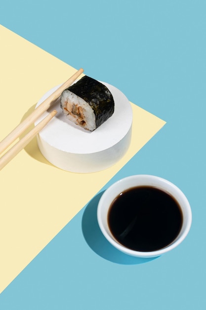 Hosomaki-sushibroodjes met paling en sojasaus op een witte gipstribune op een kleurrijke effen achtergrond blauwgeel