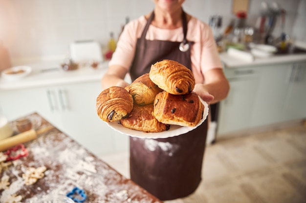 Photo hospitable woman holding plate with pastries in extended hands