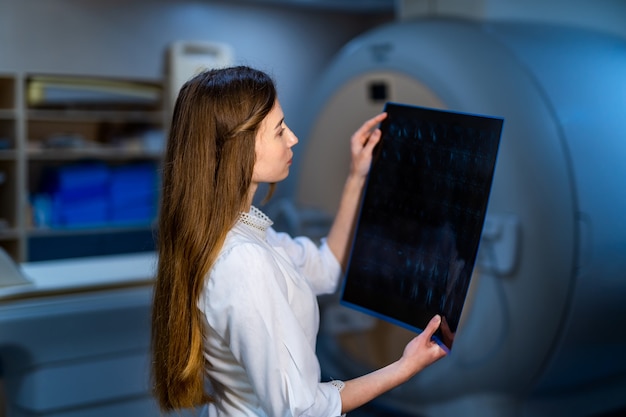 Hospital doctor holding patient's x-ray film. Modern MRI machine background. Healthcare, roentgen, people and medicine concept.