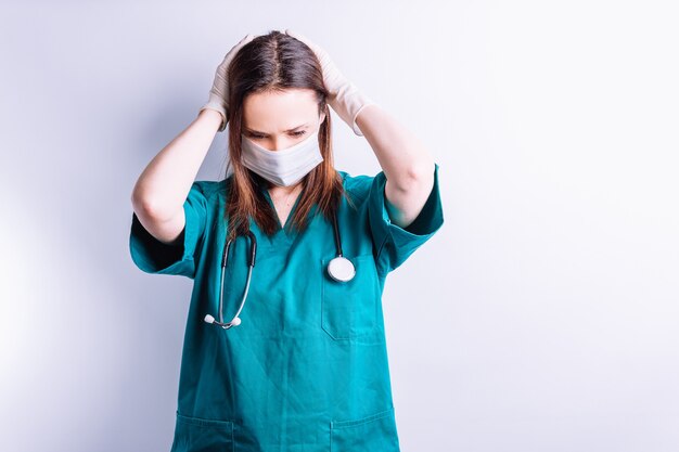 Medico ospedaliero con maschera facciale e stetoscopio con le mani sulla testa guardando in basso. concetto disperazione depressione