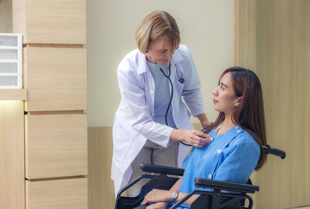 В коридоре больницы улыбающийся доктор осматривает пациента азиатскую женщину, парализованную