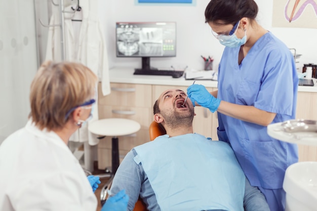 Hospital nurse in medical uniform looking into sick pacient mouth analyzing teeth health preparing for stomatological surgery