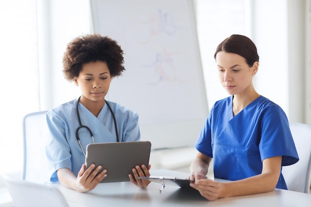 Hospital, profession, people and medicine concept - doctors\
with tablet pc computer and clipboard meeting at medical\
office