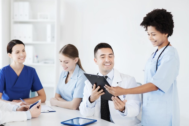 Photo hospital, profession, people and medicine concept - group of happy doctors with clipboard meeting and discussing something at medical office