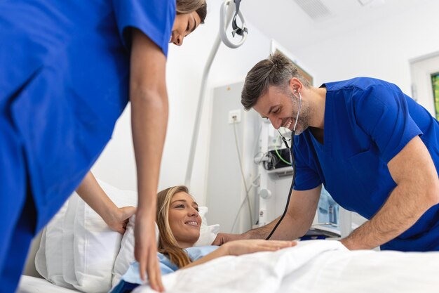 Hospital Ward Friendly Doctor and nurse taking care of Beautiful Caucasian Female Patient Resting in Bed Physician explains Test Results Woman Recovering after Successful Surgery