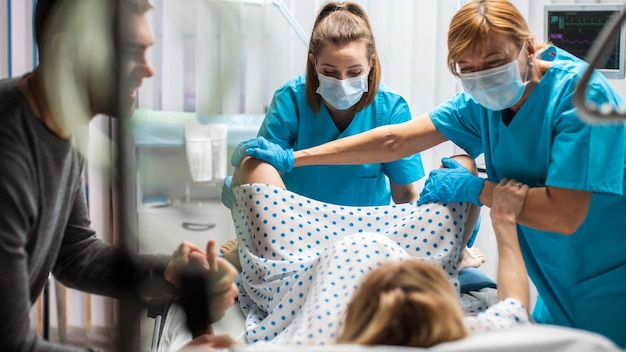in the hospital woman giving birth husband holds her hand in support obstetricians assisting modern delivery ward with professional midwives