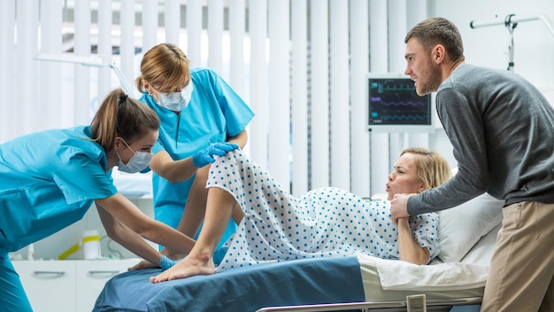 Photo in the hospital woman in labor gives birth obstetricians and doctors assist her husband supports her by holding hand modern technologically advanced maternity ward with professional midwives