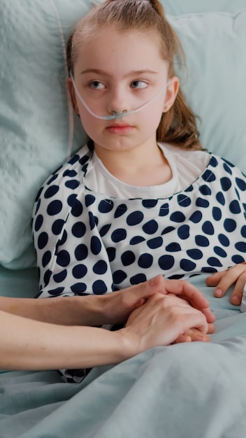 Hospitalized child wearing oxygen nasal tube resting in bed with medical oximeter on finger