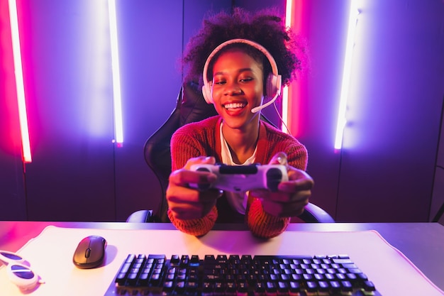 Host channel of gaming streamer african girl playing online game with joystick talking with viewers media online on microphone esport skilled team players in neon color lighting room tastemaker