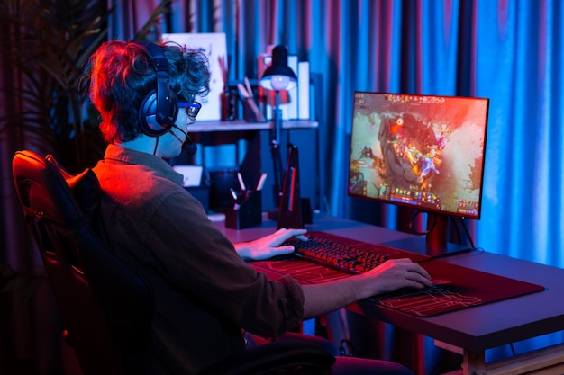 host channel of young gaming streamer playing fighting moba at battle arena game with multiplays team wearing headphone on pc monitor with back side image at neon digital light modern room gusher
