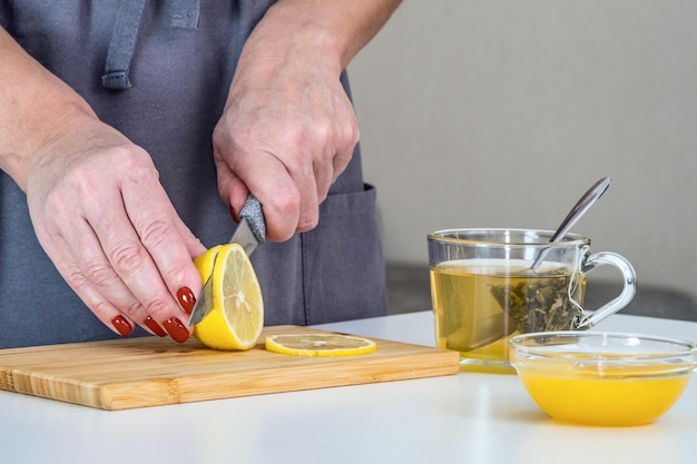 La padrona di casa prepara il tè vitaminico, taglia una fetta di limone. il tè con limone e miele aumenterà l'immunità durante una pandemia. protezione contro il coronavirus.