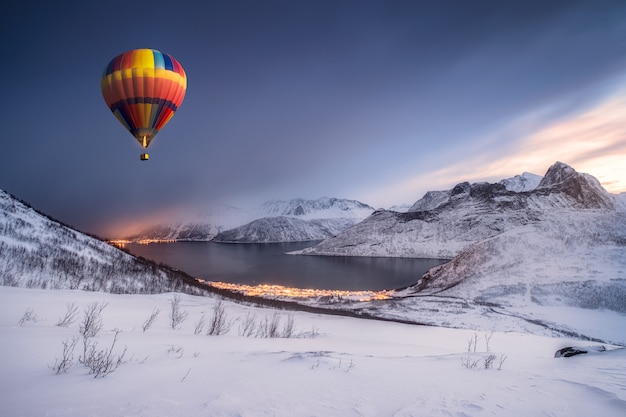 Photo hot air balloon flying on snow hill with fordgard town in winter