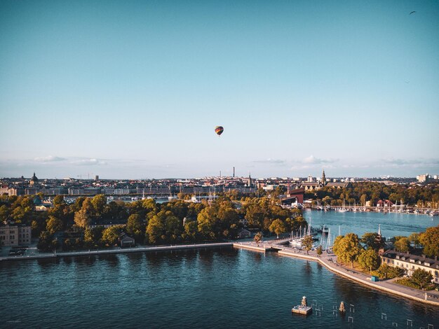 Photo hot air balloons flying over river and buildings in city