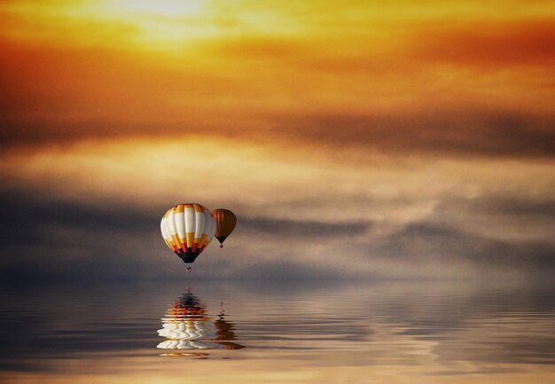 Hot air balloons in sea against sky during sunset