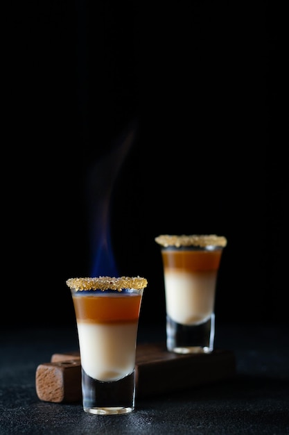 Hot alcoholic shot with baileys and whiskey with fire on a black background closeup