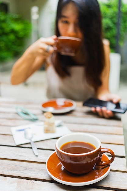 Горячий кофе americano в чашке с азиатской женщиной пить кофе в кафе.