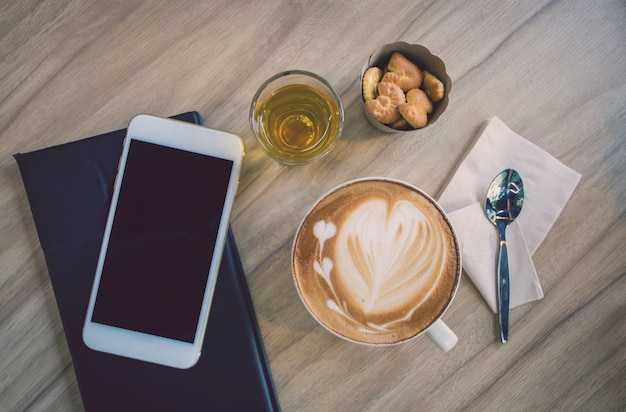 コーヒーショップの木製テーブルの上のカップでホットアートラテコーヒーは、背景をぼかし。