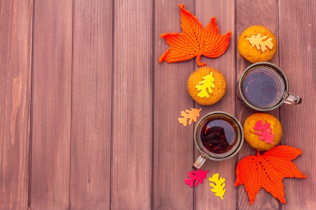 Hot autumn drink. black tea with cupcakes, colorful leaves