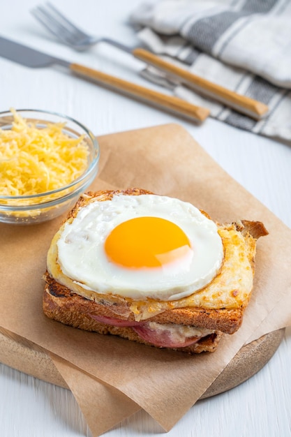 Hot baked Croque Madame sandwich with ham and cheese topped with fried egg on paper on table