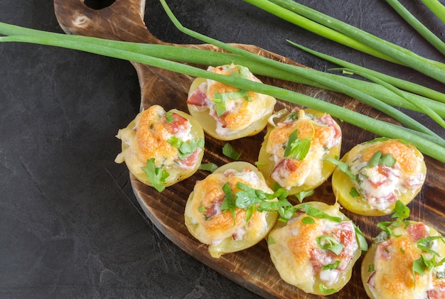 Patate ripiene al forno calde con formaggio, pancetta, prezzemolo su una tavola di legno.