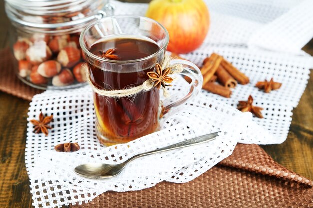 Hot beverage in glass cup with fruits and spices, on wooden background