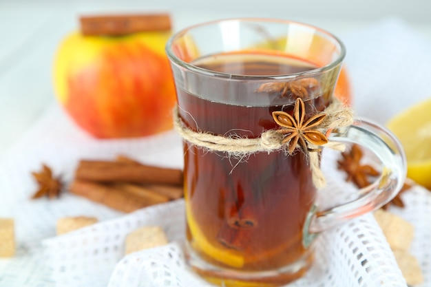 Hot beverage in glass cup with fruits and spices, on wooden background
