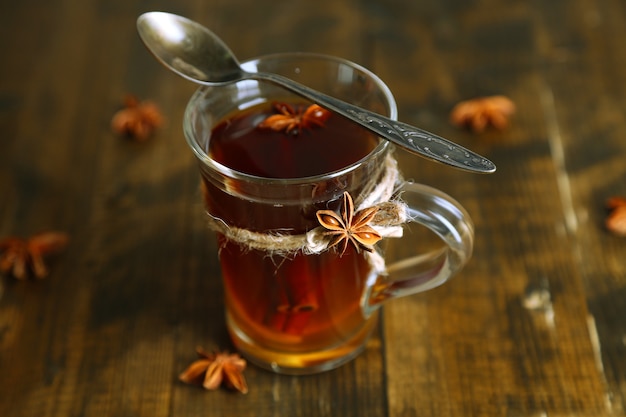 Hot beverage in glass cup with fruits and spices, on wooden surface