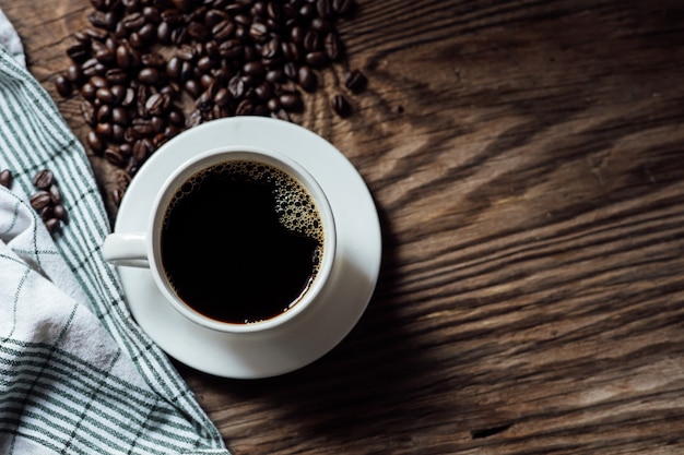 Hot black coffee cup and coffee beans on wooden table with natural light in the morning. Top view coffee cup