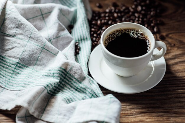 Tazza di caffè nero e chicchi di caffè caldi sulla tavola di legno con luce naturale di mattina