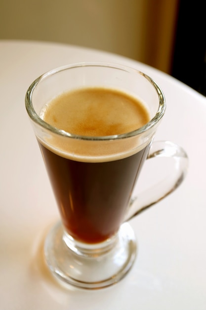 Hot black coffee in a transparent glass served on white round table