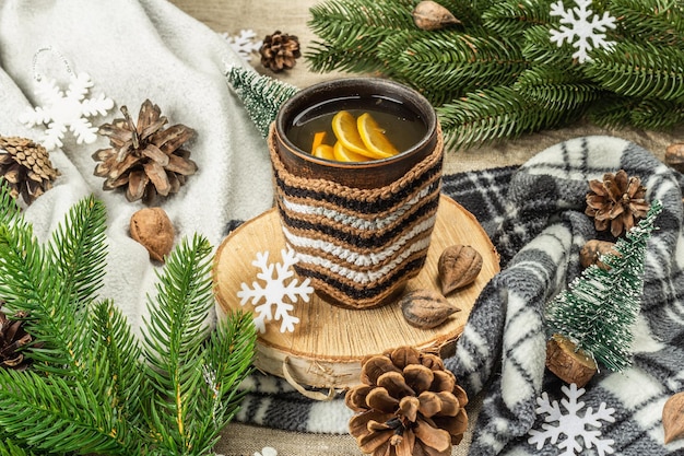 Hot black tea and lemon with winter decor. Cozy sweater, fir tree branches, nuts, snowflakes. Festive seasonal arrangement, good mood concept, rustic style