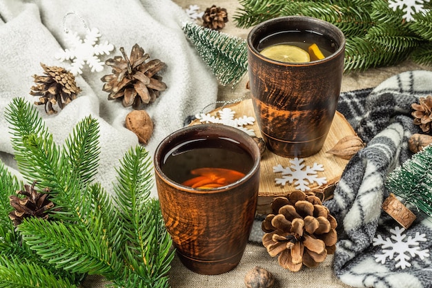 Hot black tea and lemon with winter decor. Cozy sweater, fir tree branches, nuts, snowflakes. Festive seasonal arrangement, good mood concept, rustic style