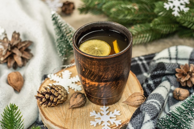 Hot black tea and lemon with winter decor. Cozy sweater, fir tree branches, nuts, snowflakes. Festive seasonal arrangement, good mood concept, rustic style