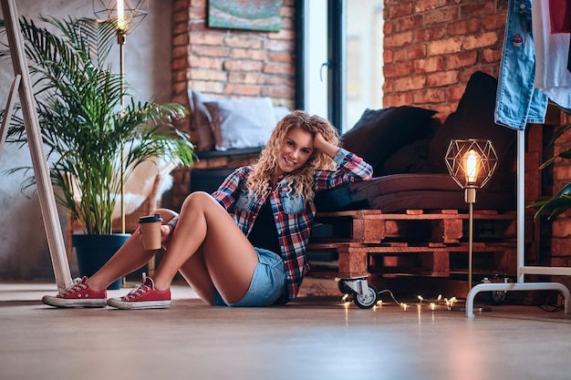 A hot blonde female dressed in denim shorts and fleece shirt posing in a studio with loft background.