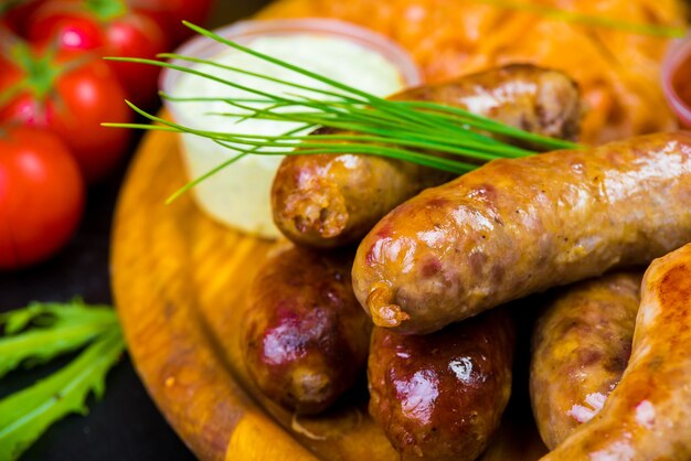 Photo hot browned ruddy homemade sausages on a wooden tray with sauces and vegetables